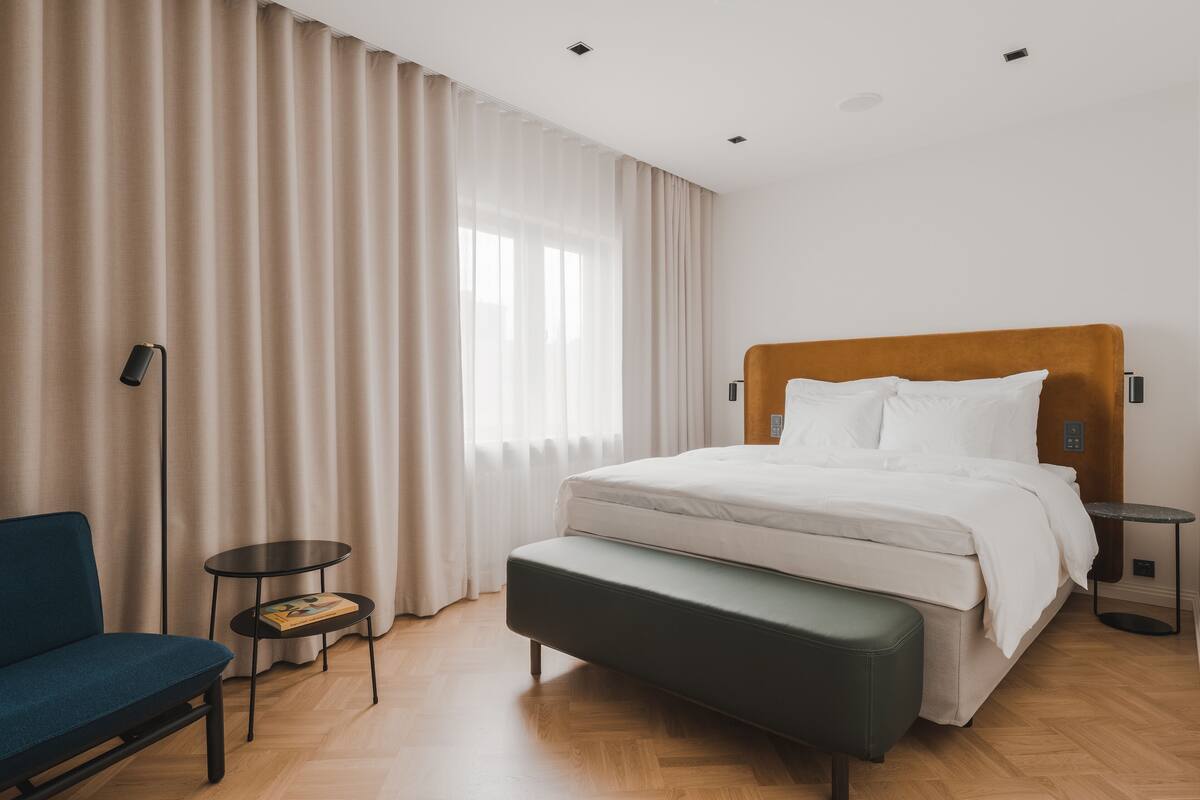 Ein modernes Hotelzimmer mit einem großen Bett, einer Bank, einem kleinen Tisch und einem Stuhl.