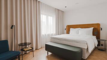 Una habitación de hotel moderna con una cama grande, un banco, una mesita y una silla.