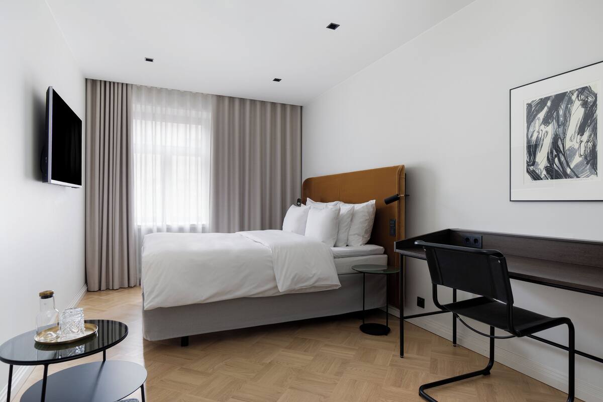 Ein modernes Hotelzimmer mit einem Bett, einem Schreibtisch, einem Sessel, einem Fernseher und Kunstwerken an der Wand.