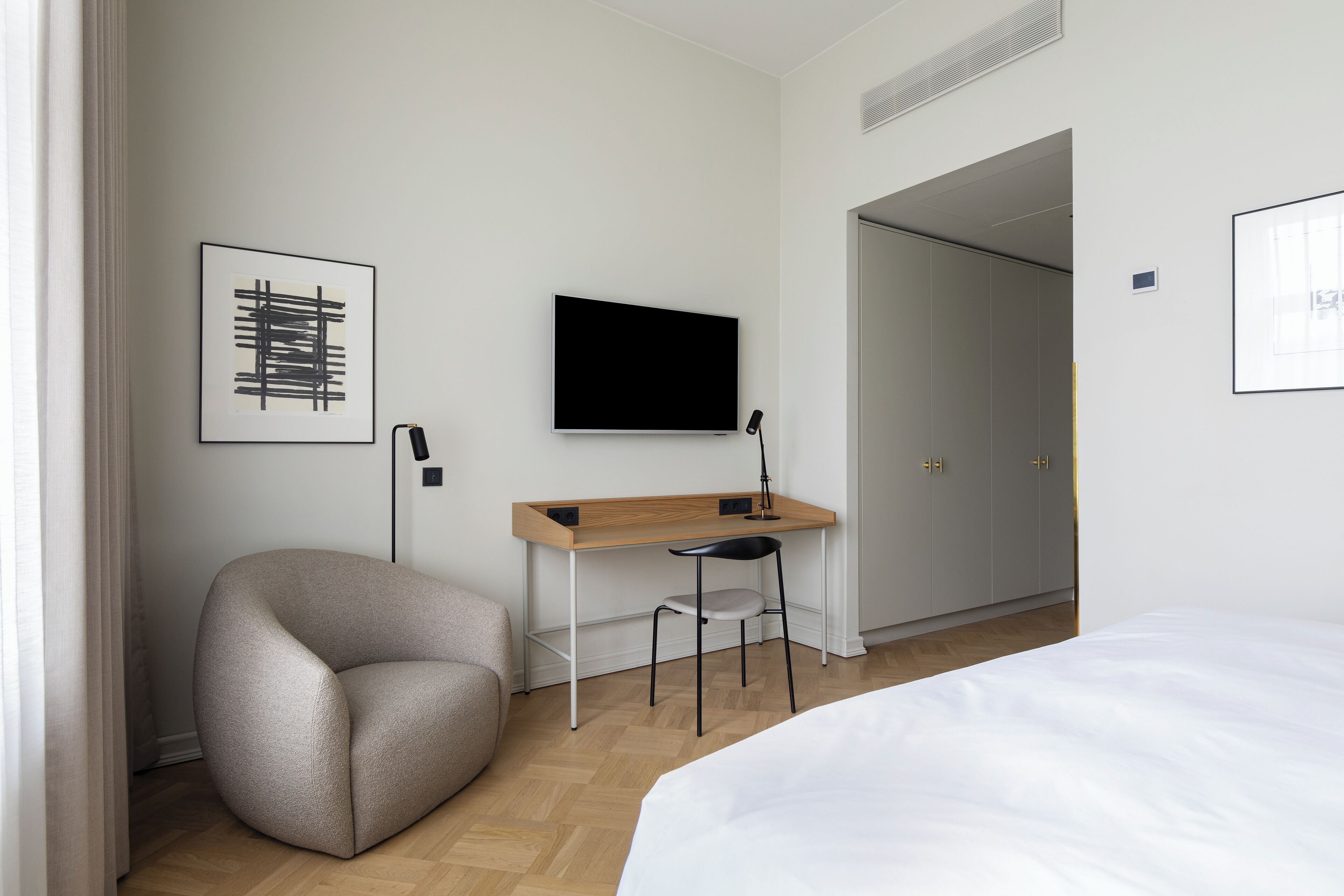 Habitació d'hotel moderna amb un llit, una taula de treball amb una cadira, un televisor de pantalla plana i un armari.