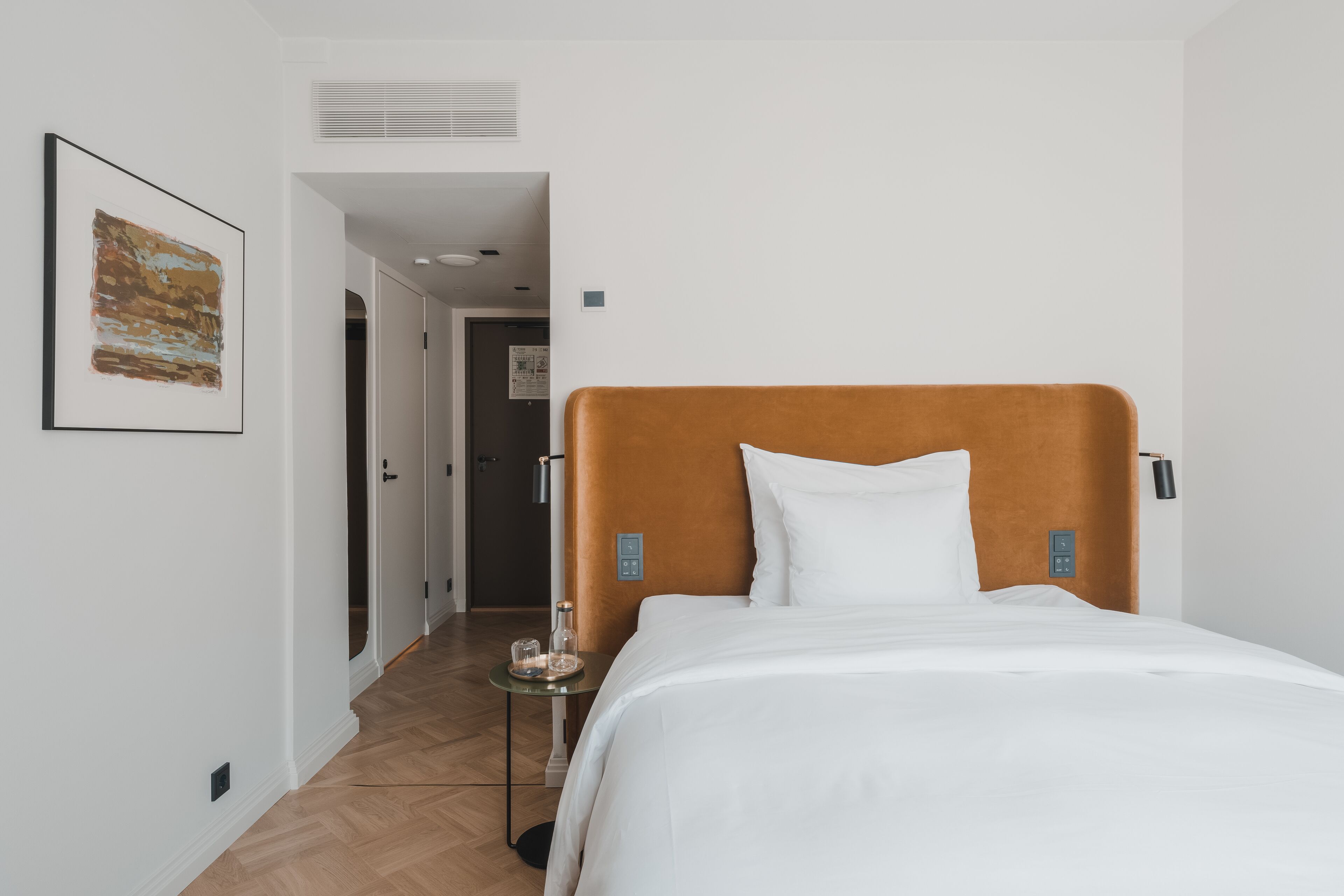 Een hotelkamer met een groot bed, een klein nachtkastje, een inlijsting foto aan de muur en een deur naar een andere kamer.