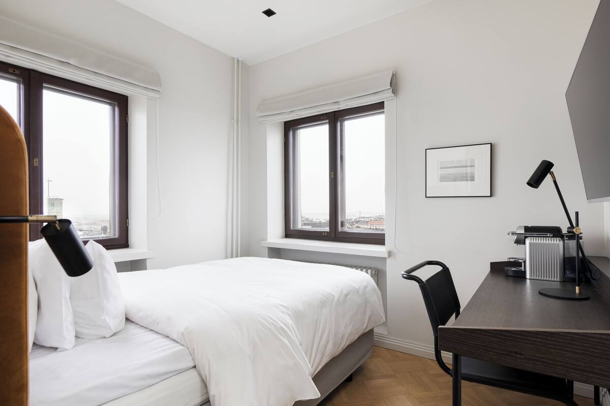 Ein Hotelzimmer mit Bett, Schreibtisch mit Lampe und Blick aus dem Fenster.