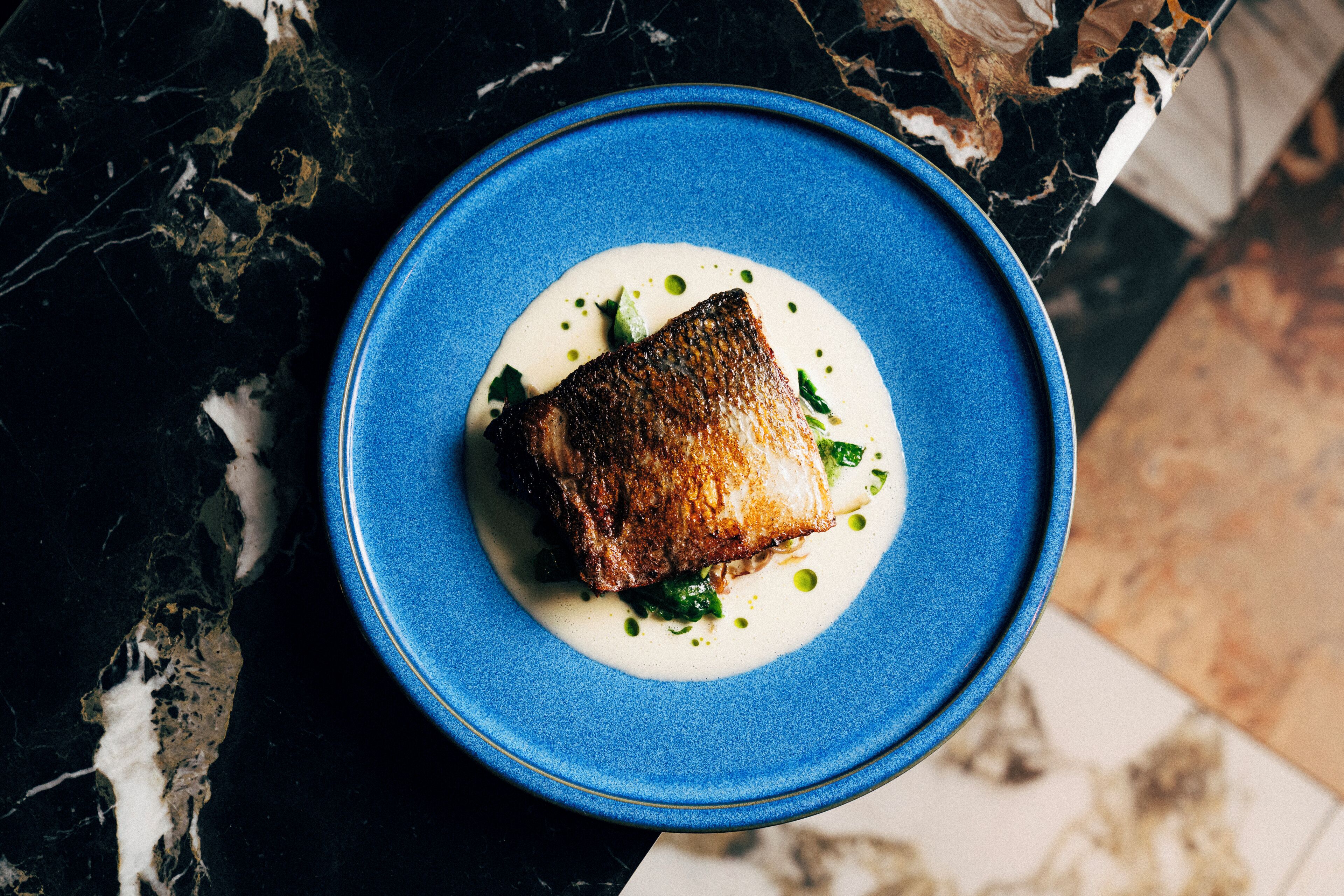 Une assiette bleue sur laquelle se trouve un morceau de nourriture, le tout posé sur une surface en marbre.
