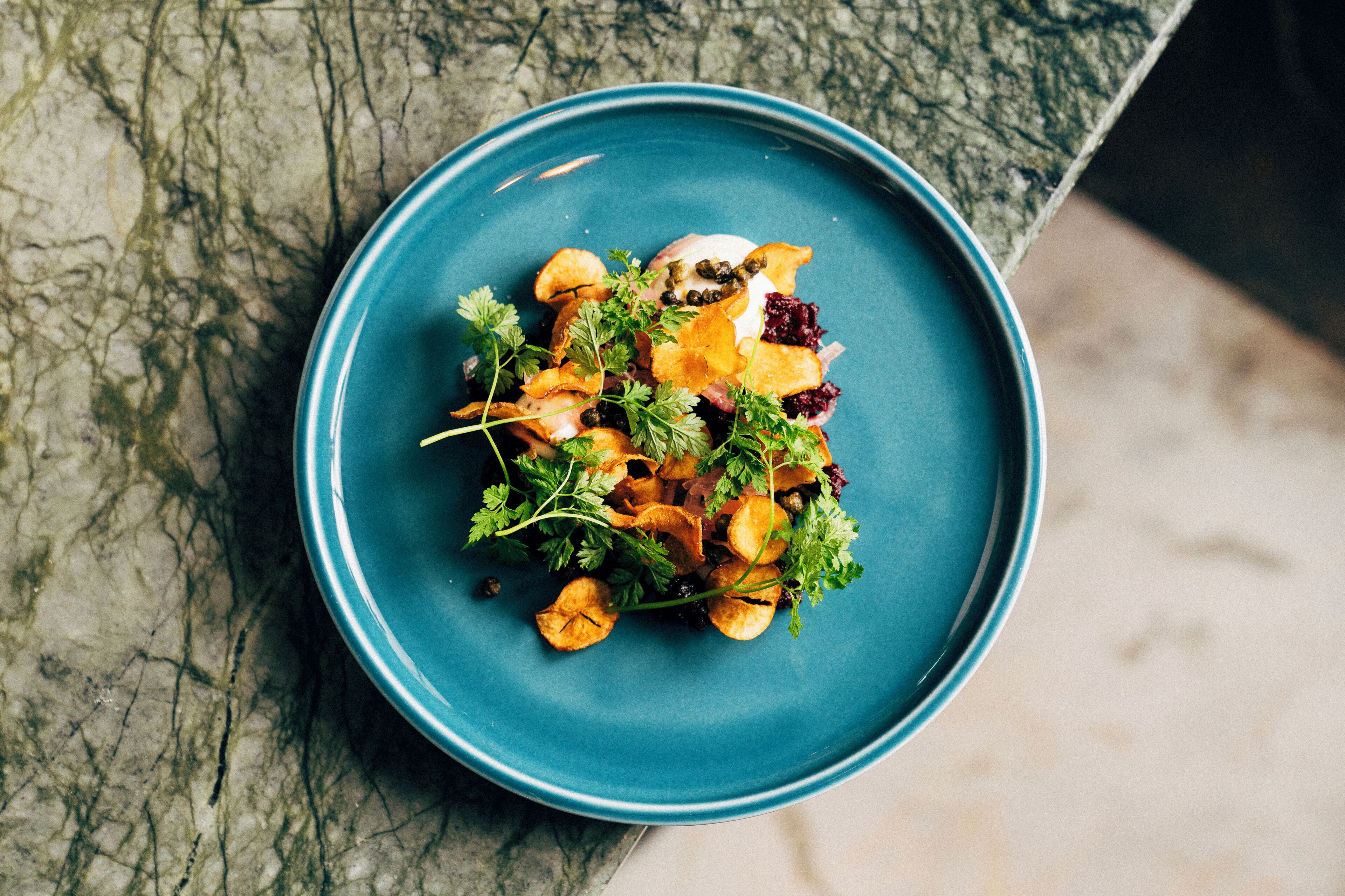 A blue plate with a salad on a marble surface.
