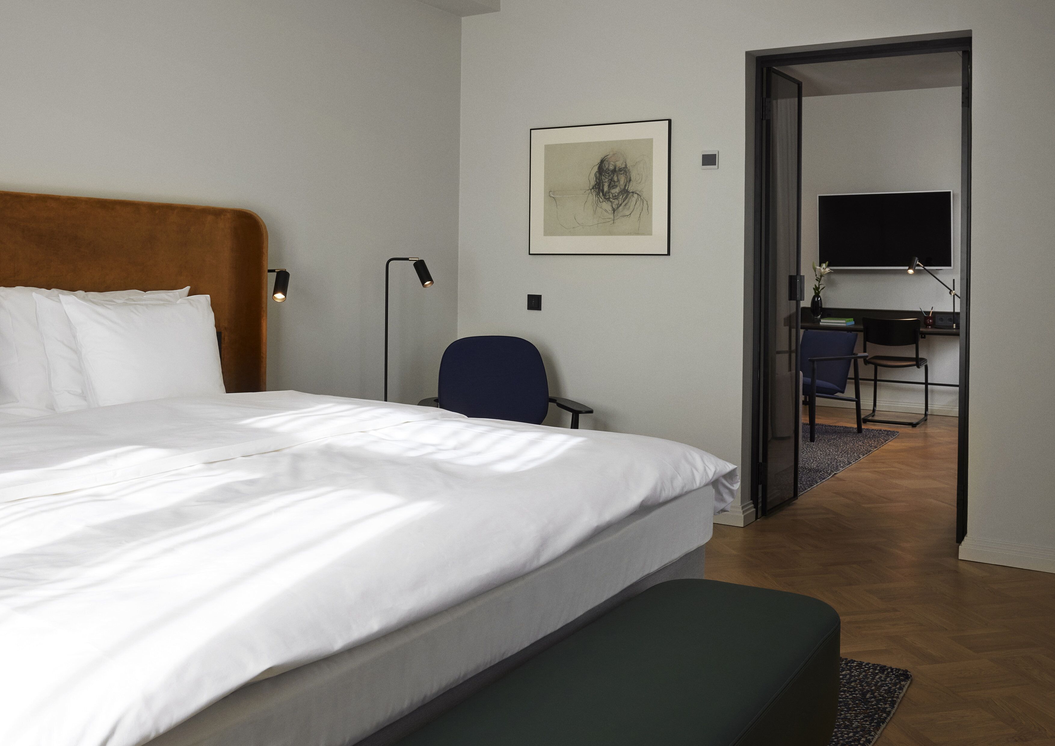 Quarto de hotel com uma cama grande, uma escrivaninha, uma cadeira e uma televisão no quarto ao lado.
