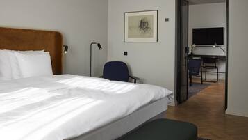 Quarto de hotel com uma cama grande, uma escrivaninha, uma cadeira e uma televisão no quarto ao lado.