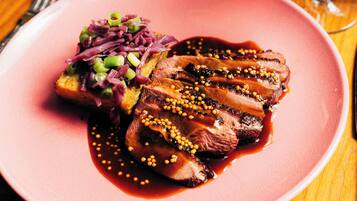 A pink plate with sliced meat, a side of red cabbage, and a piece of toast.