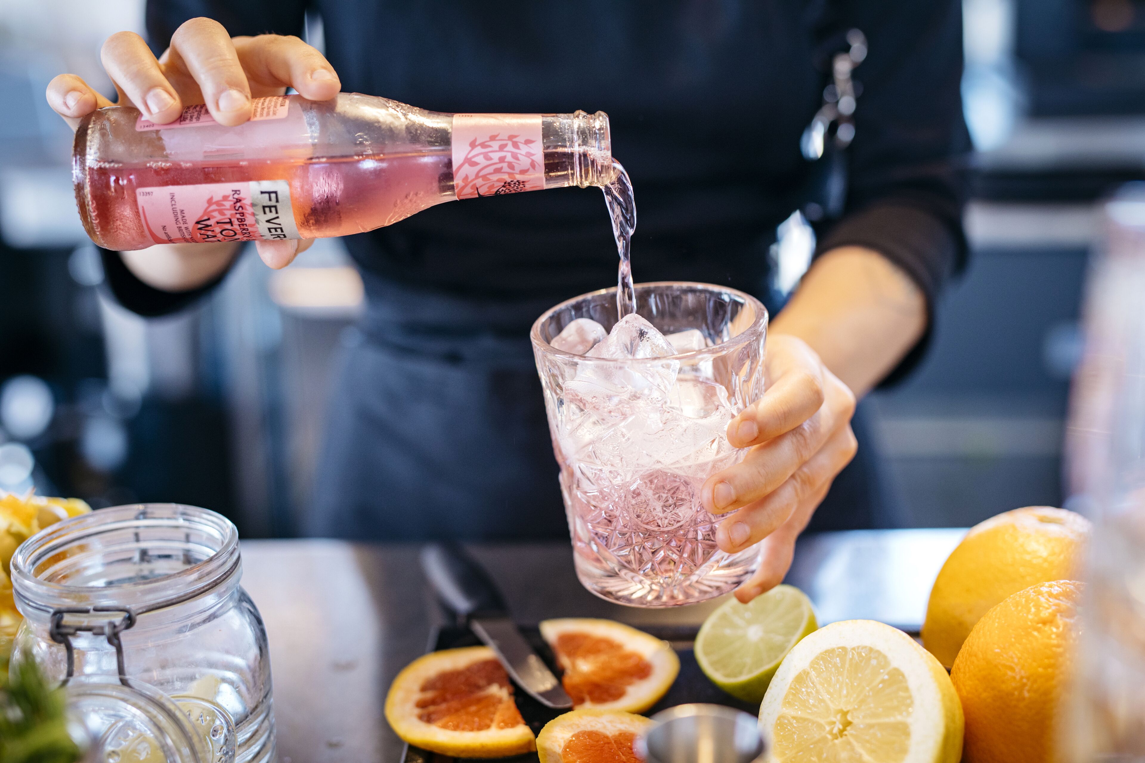 A person pouring a pink liquid into a glass with ice cubes.