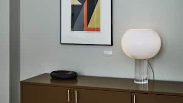 A framed abstract artwork, a modern table lamp, and a brown cabinet with a black object on top.
