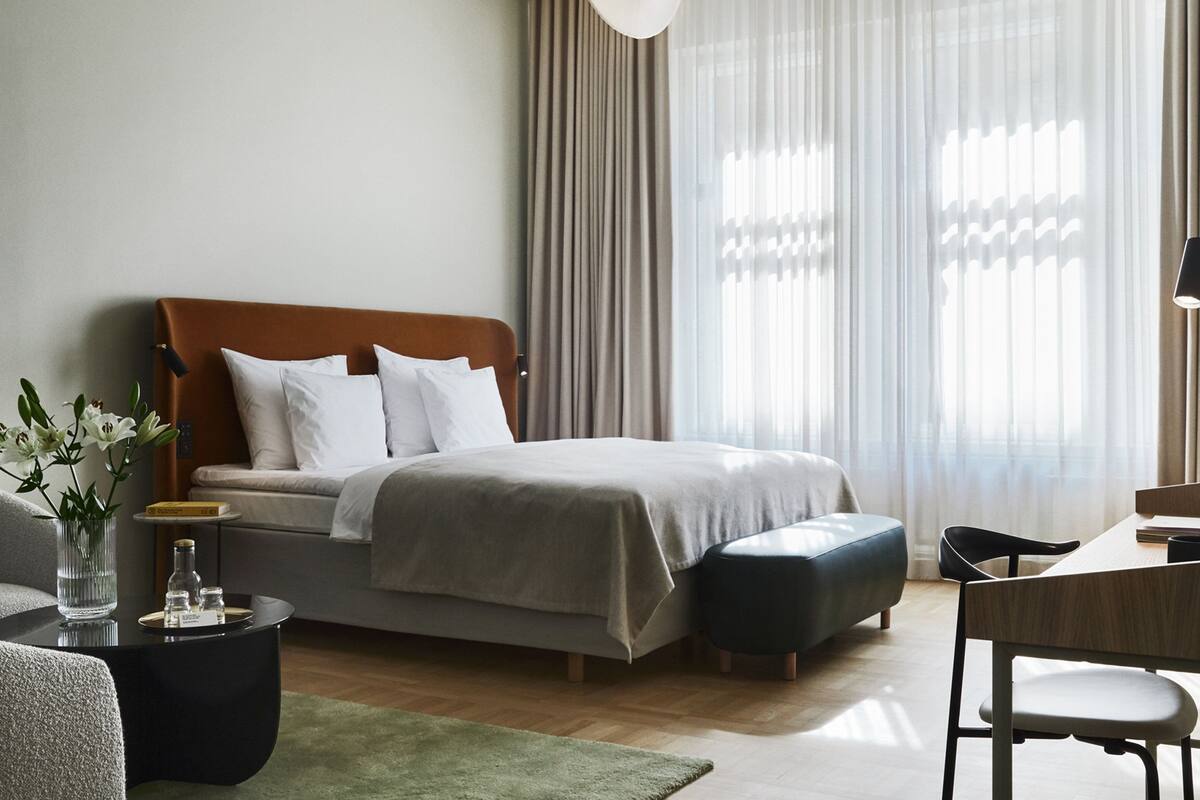 Ein modernes Hotelzimmer mit Bett, Schreibtisch, Stuhl, einer Vase mit Blumen und einer Lampe.