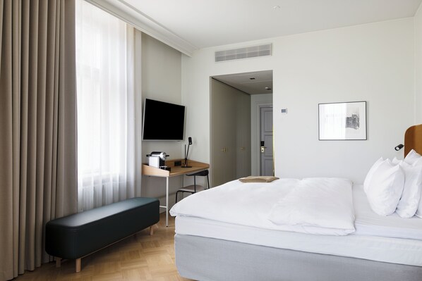 Una camera d'albergo con un letto, una scrivania, una panca, una TV e una porta che dà su un'altra stanza.