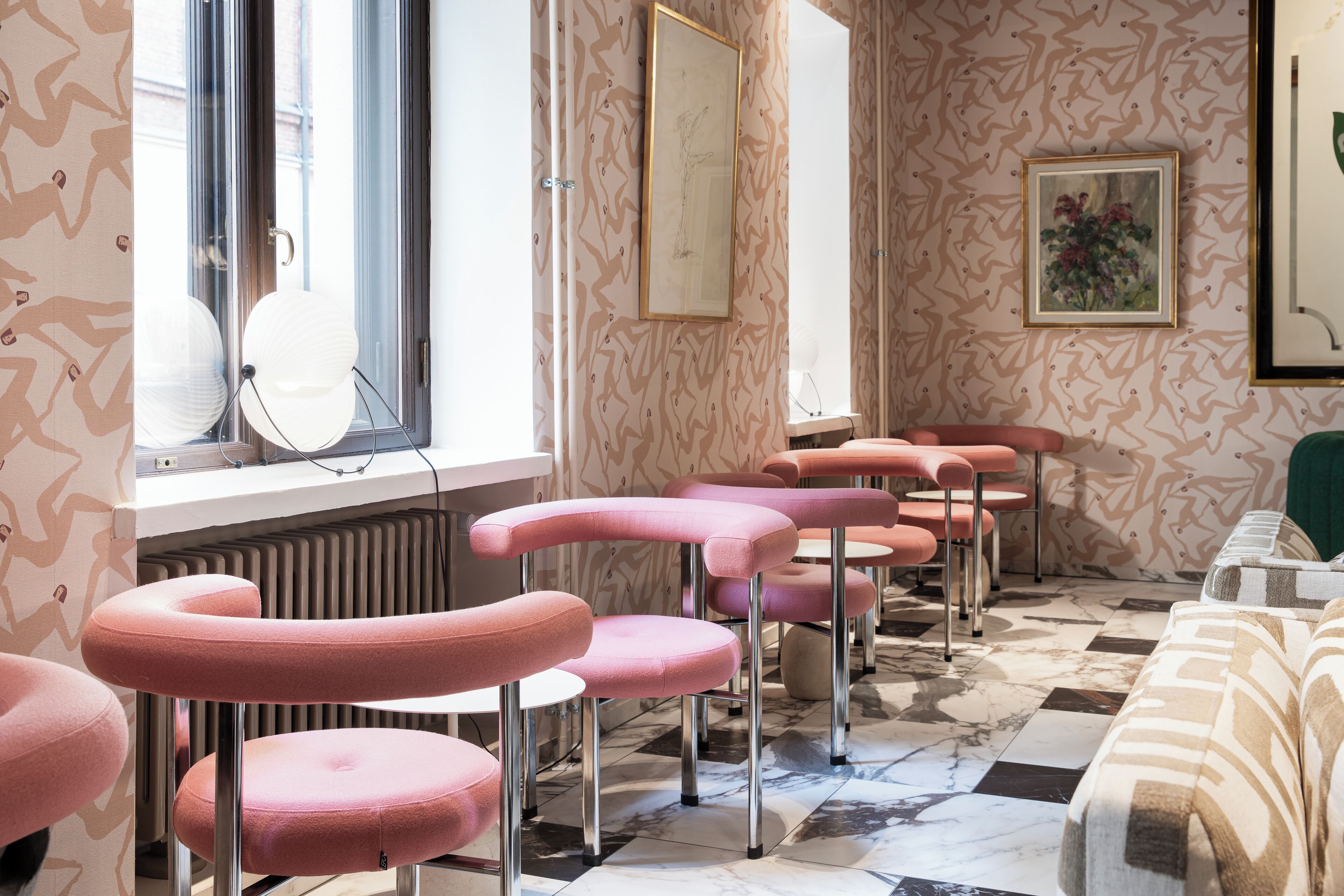 A salon with pink chairs, a radiator, and patterned wallpaper.
