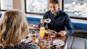 Desayuno con vistas a la ciudad, una mesa con diversas opciones para el desayuno, y una persona sosteniendo una taza.