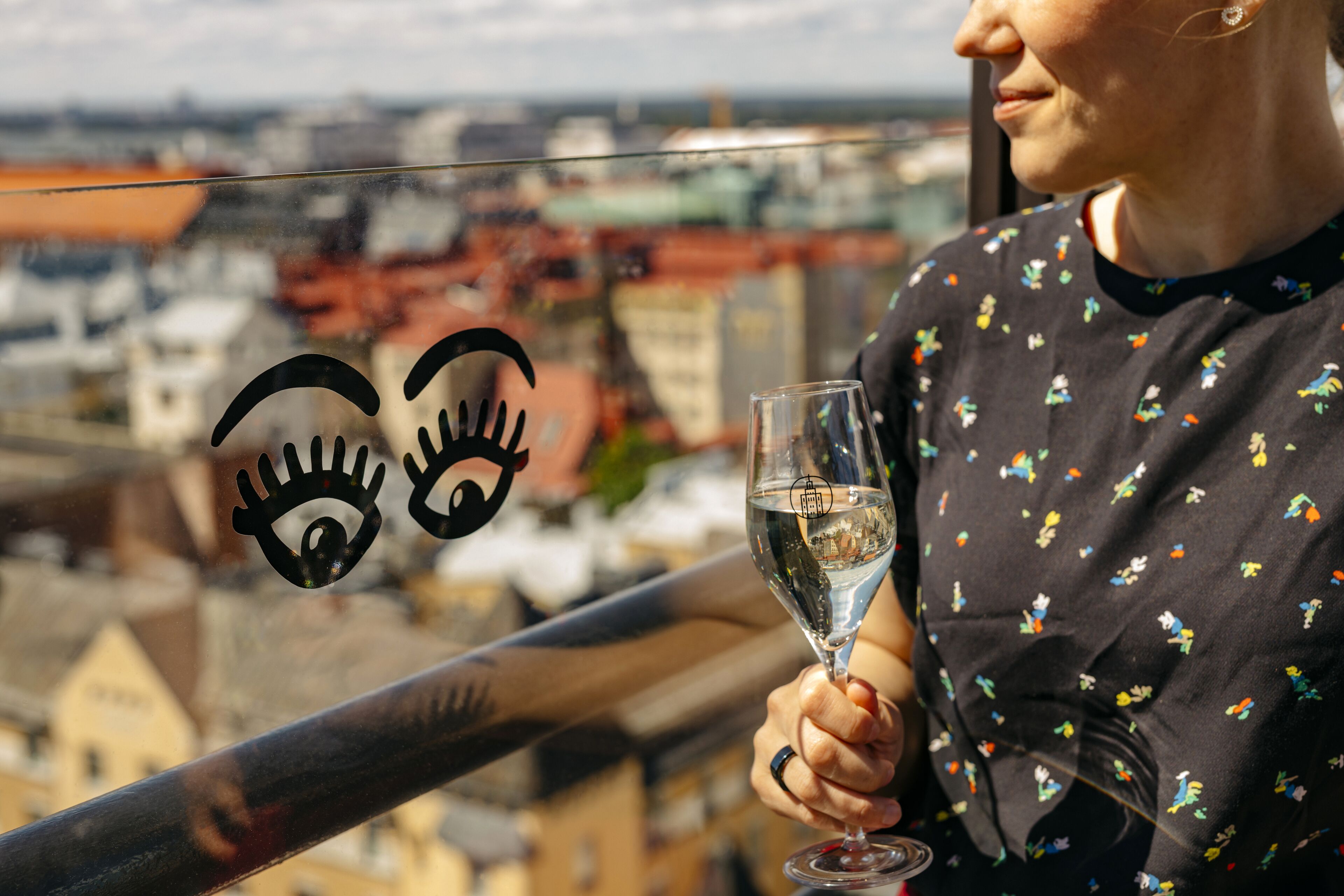 A person holding a glass of white wine, overlooking a cityscape with buildings.