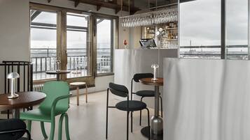 Un espace de restauration moderne offrant une vue sur la ville, avec un bar doté d’un présentoir à bouteilles, de nombreux types de sièges et une grande fenêtre.
