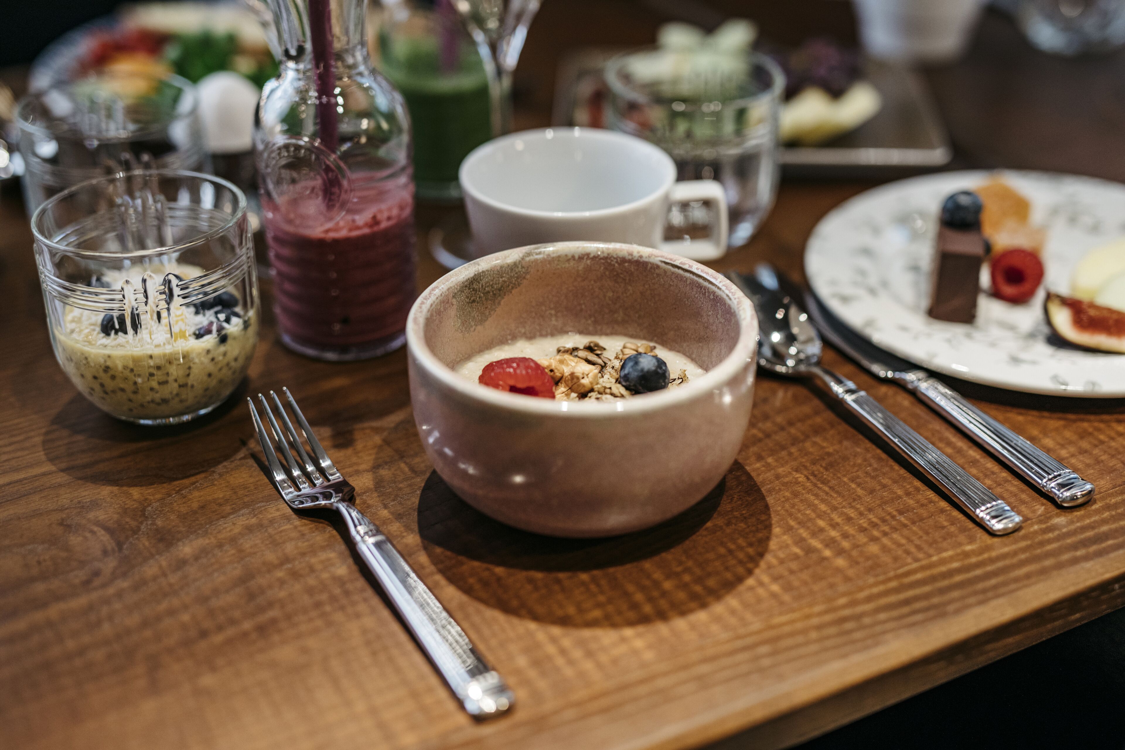 A breakfast setting with a bowl of cereal, a glass of smoothie, and a plate with pastries.