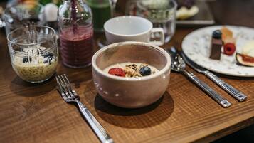 A breakfast setting with a bowl of cereal, a glass of smoothie, and a plate with pastries.