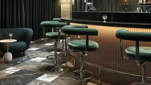 Una zona de bar con una barra curva, taburetes verdes y una vitrina de cristal.