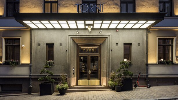 Entrada de un hotel con fachada oscura, ventanas iluminadas y un cartel que dice "TORNI".