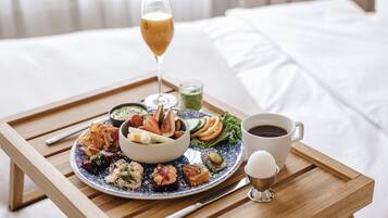 A tray with a variety of foods, a glass of drink, and a cup of coffee on a wooden table in a hotel room.