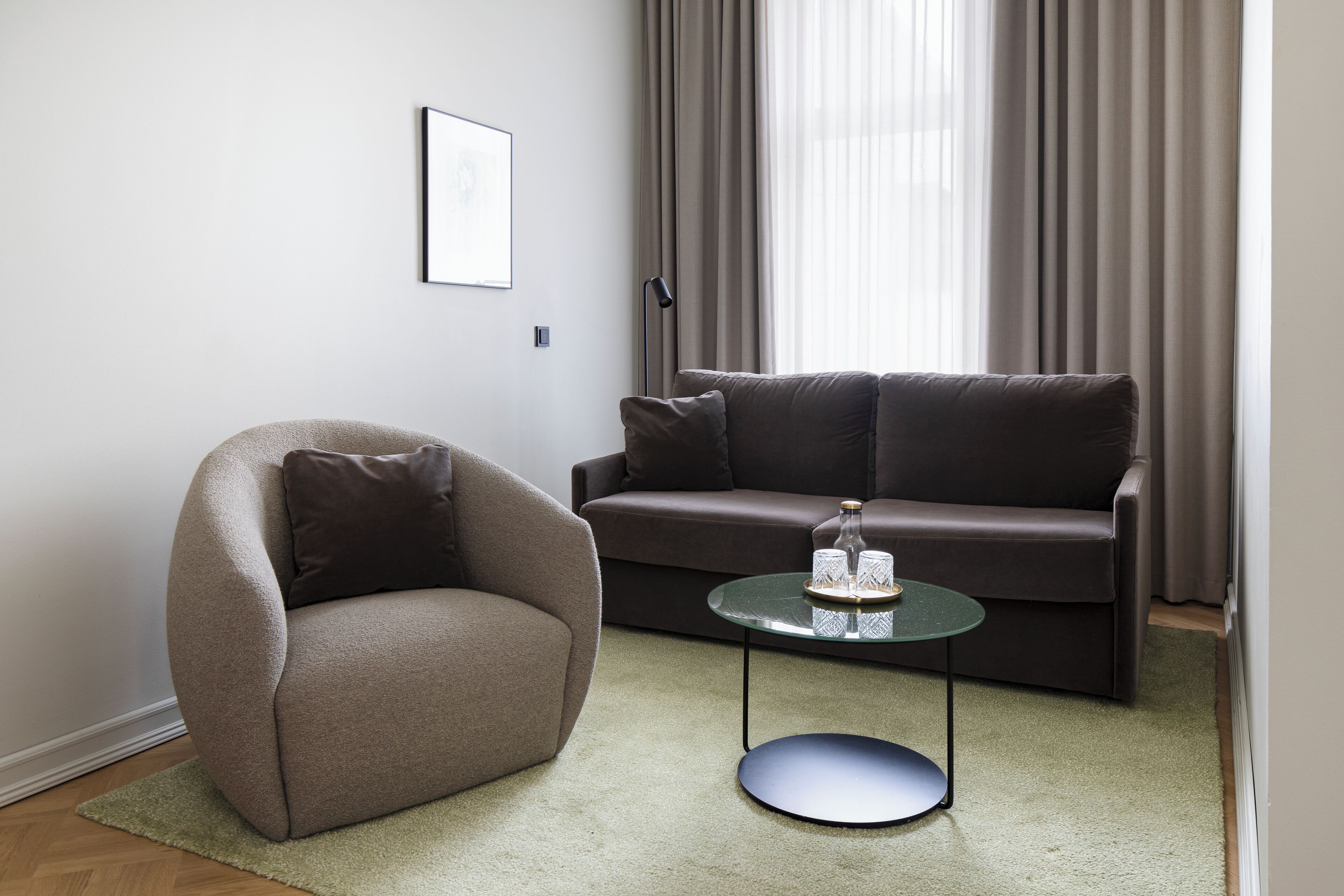 Un salon moderne avec un fauteuil marron, un canapé brun foncé et une table basse en verre agrémentée d’objets décoratifs.