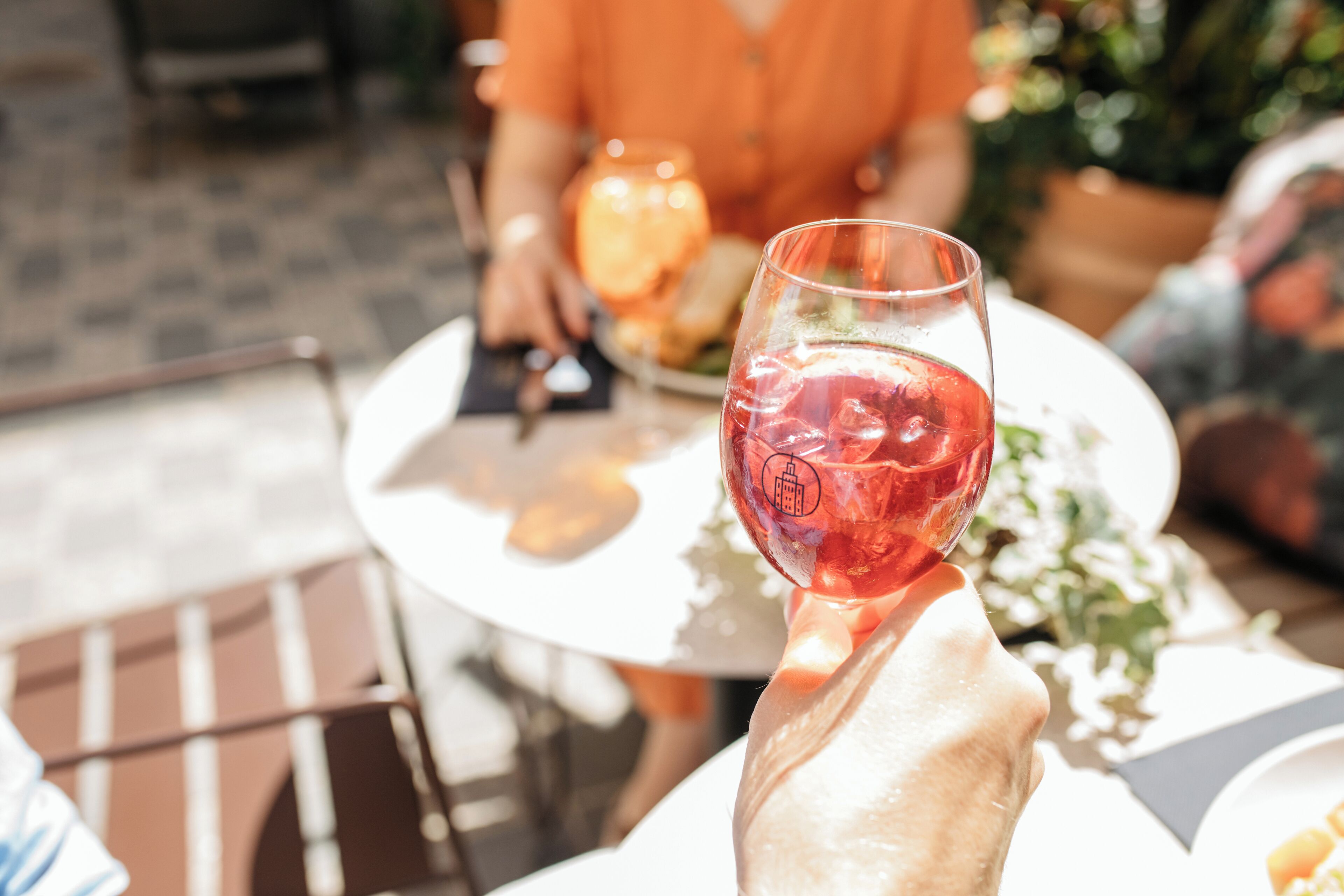A person holding a wine glass at an outdoor table with a plate of food and a glass of water.