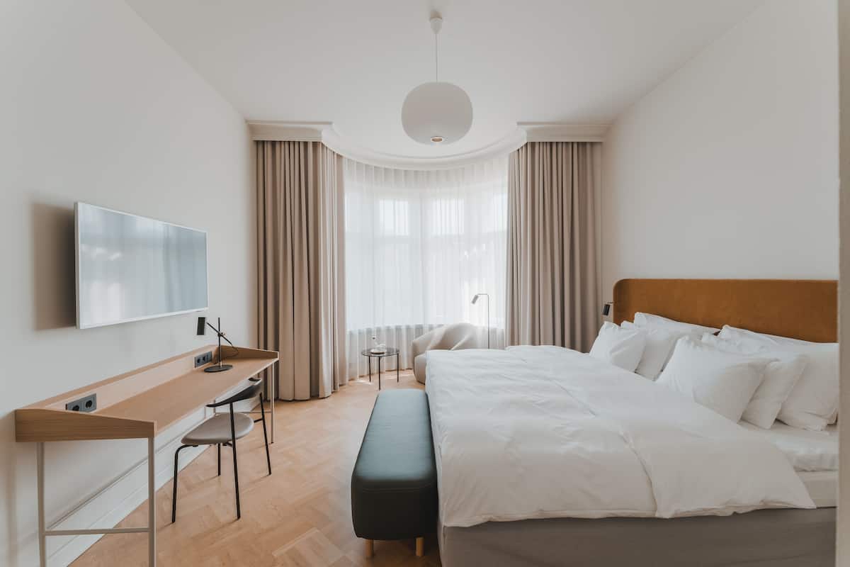Ein Hotelzimmer mit einem Bett, einem Schreibtisch mit Stuhl, einem Fernseher und einem Fenster mit Vorhängen.