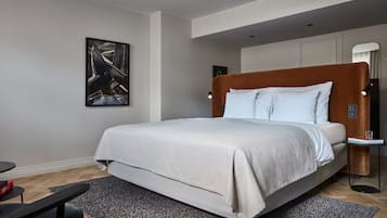 A modern bedroom with a large bed, a side table, a floor lamp, and a painting on the wall.