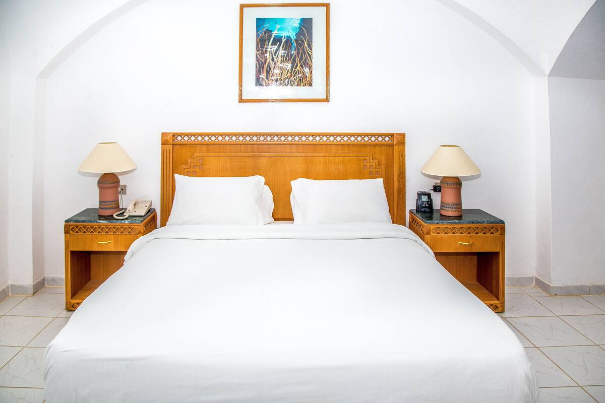 A neatly made bed with white linens, two wooden nightstands with lamps, and a framed picture above the bed.