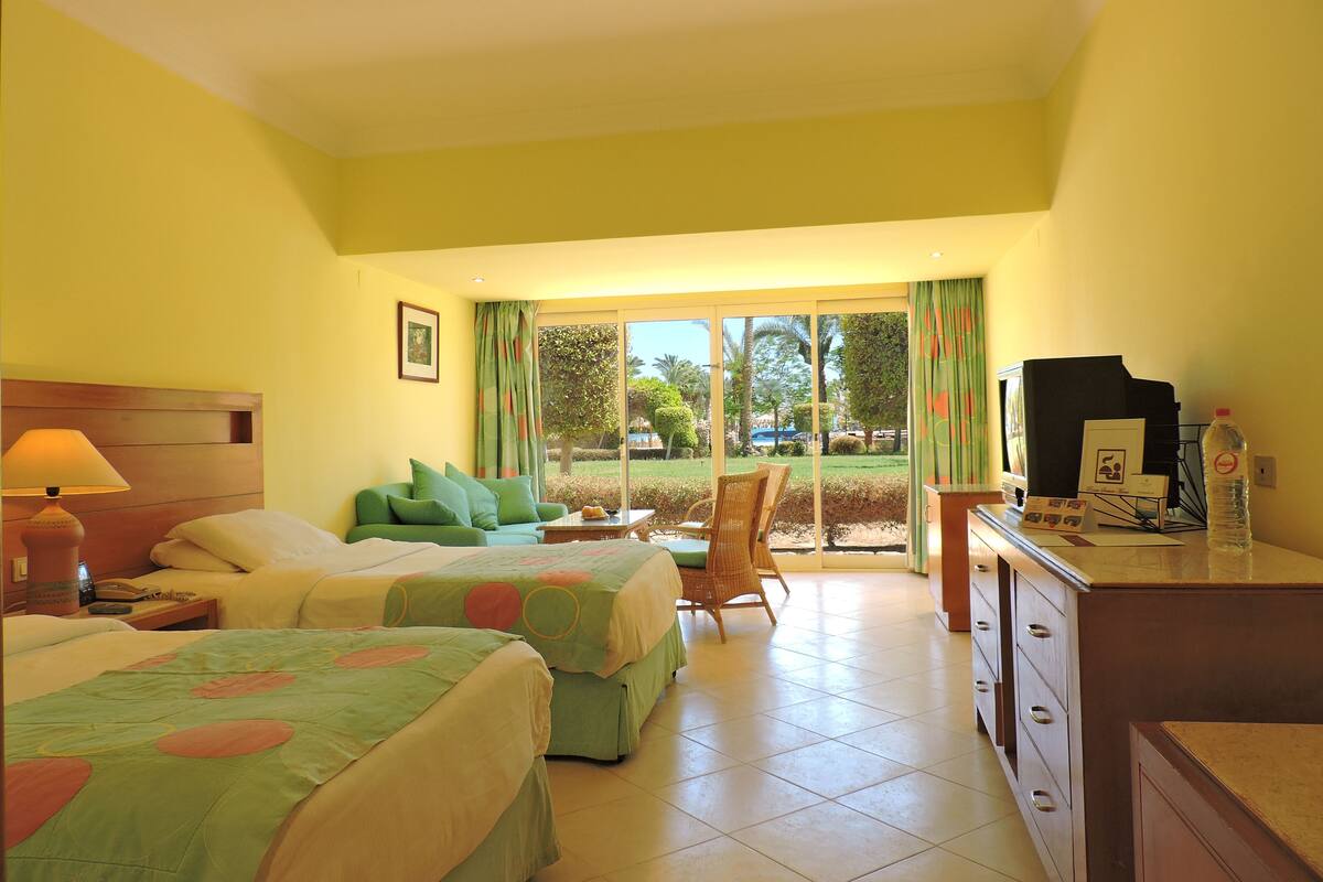A hotel room with two beds, a desk, a chair, and a view of the outdoors.