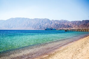 Una playa con agua turquesa cristalina, una orilla arenosa y montañas al fondo.
