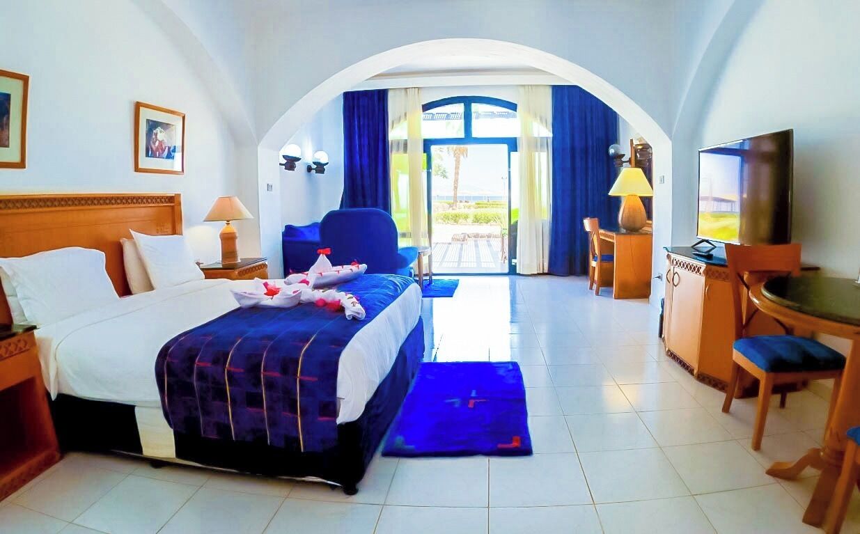 Habitación de hotel con cama, escritorio, televisión y vista al exterior a través de un acceso.