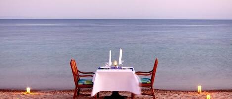 A beachside table set with candles and a white tablecloth, overlooking the sea.
