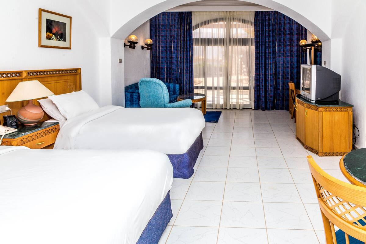 A hotel room with two beds, a TV, a desk, and a chair.