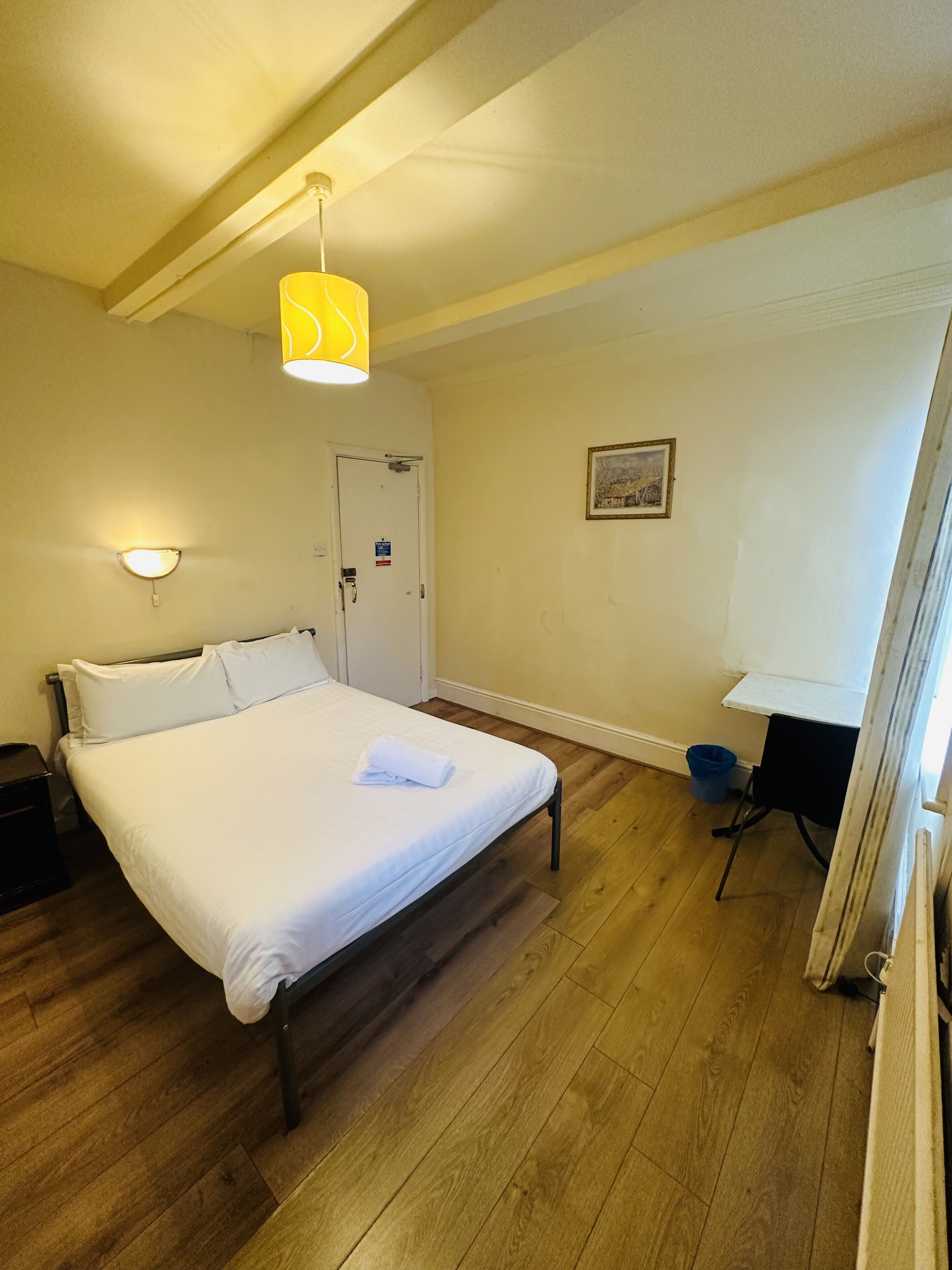 A hotel room with a bed, bedside table, lamp, and a door.