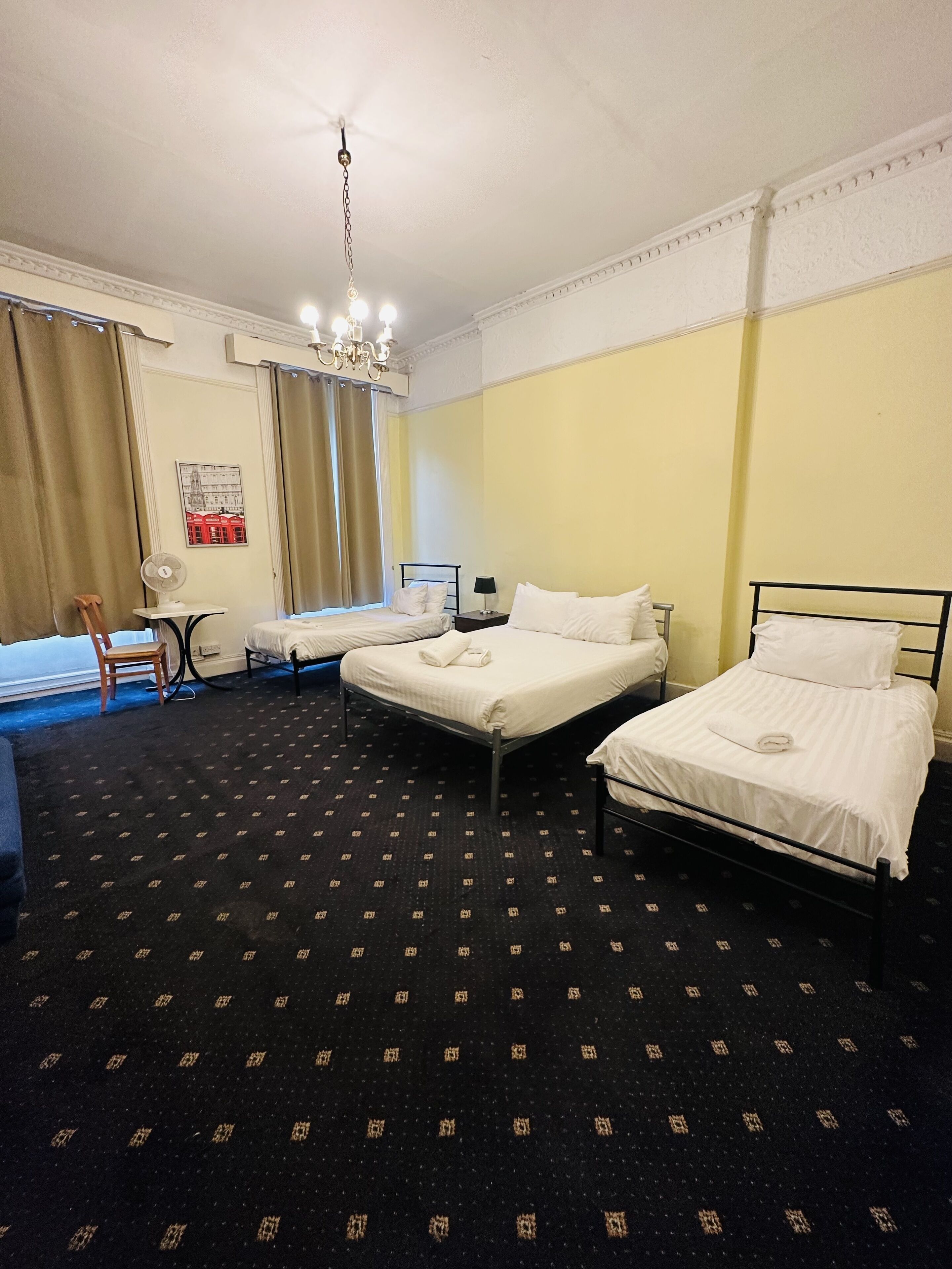 A hotel room with two beds, a desk, a chair, a fan, and a chandelier.