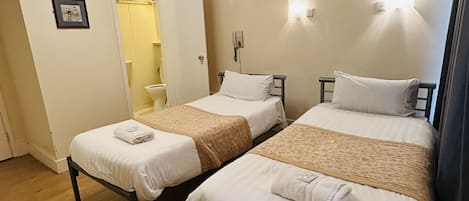 Une chambre avec deux lits, un plancher en bois, une porte blanche et un luminaire au plafond.