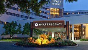 Entree van een Hyatt Regency hotel, met een modern ontwerp, grote glasramen en een aangelegde tuin met planten er voor.
