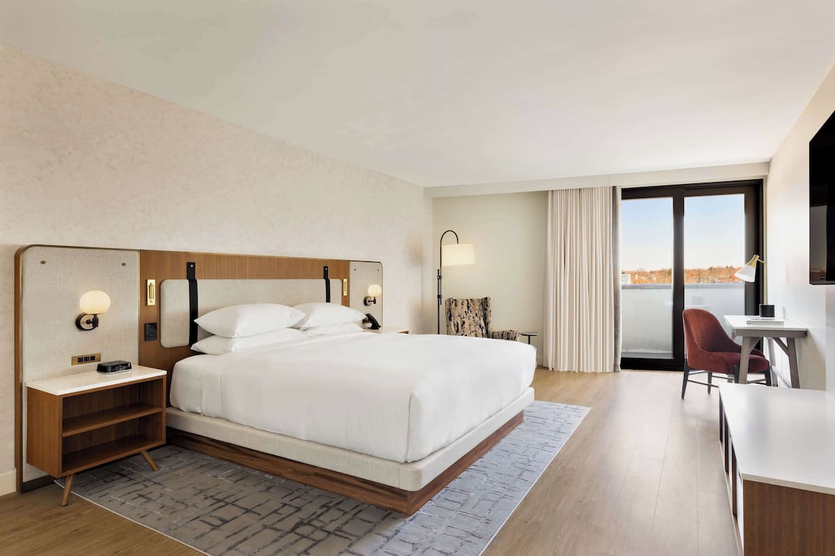 A hotel room with a large bed, bedside tables, a desk, and a view of the city.