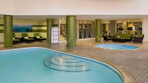 Een binnenzwembad met twee afdelingen, groene ligbedden en fitnessapparatuur op de achtergrond.