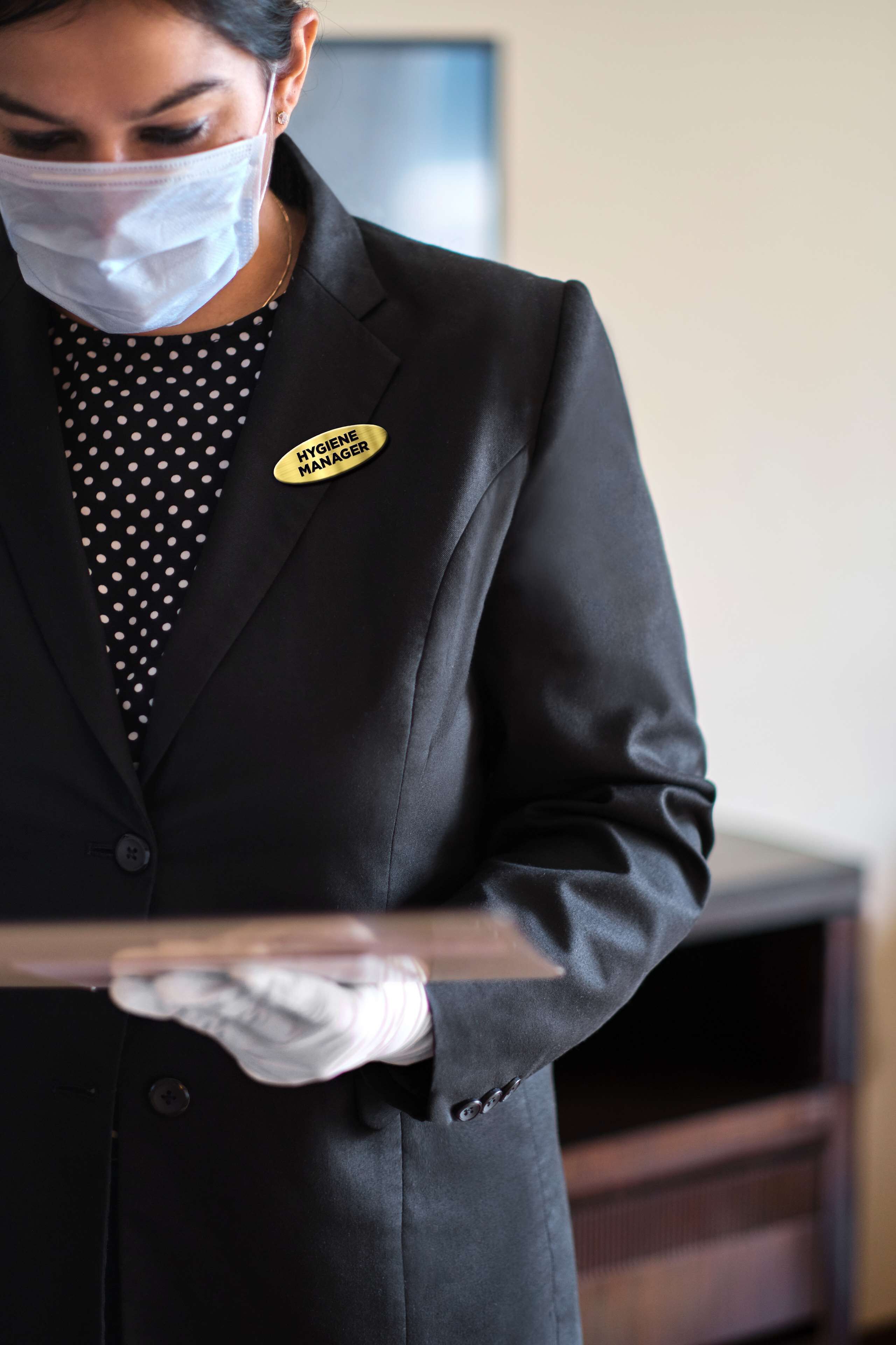A person in a black suit with a name tag reading "HYGIENE MANAGER" holding a tray.