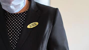 A person in a black suit with a name tag reading "HYGIENE MANAGER" holding a tray.