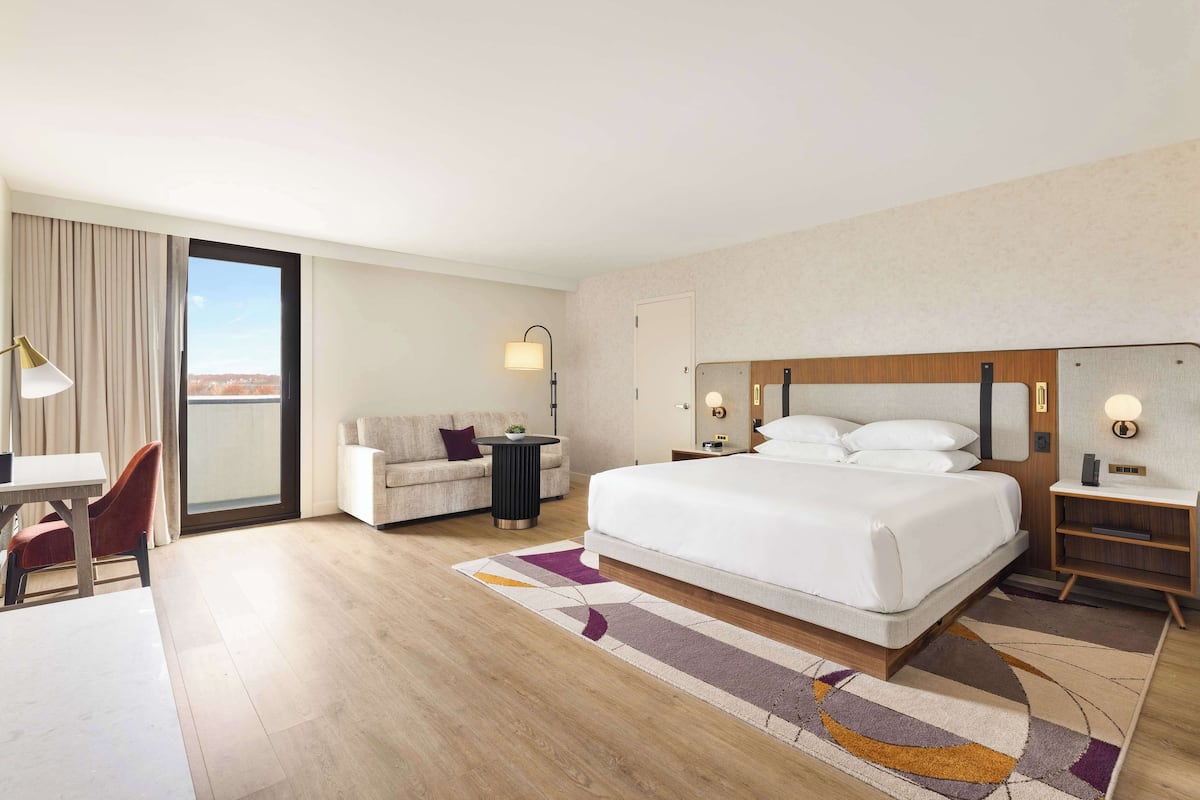 A hotel room with a large bed, a desk, a chair, a small table, and a sofa.