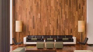 Een moderne lobby met een houten wand, een bijzondere bolvormige kroonluchter en een zithoek met sofa’s en poefs.