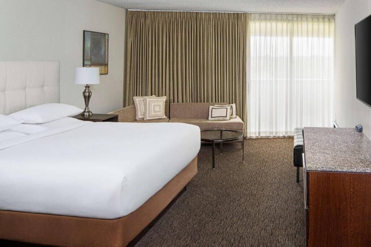 Une chambre d’hôtel avec un grand lit, un canapé, une petite table ronde, un bureau et un téléviseur.