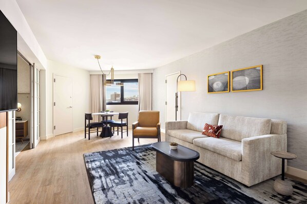 A modern living room with a sofa, coffee table, and a dining area with chairs and a table.