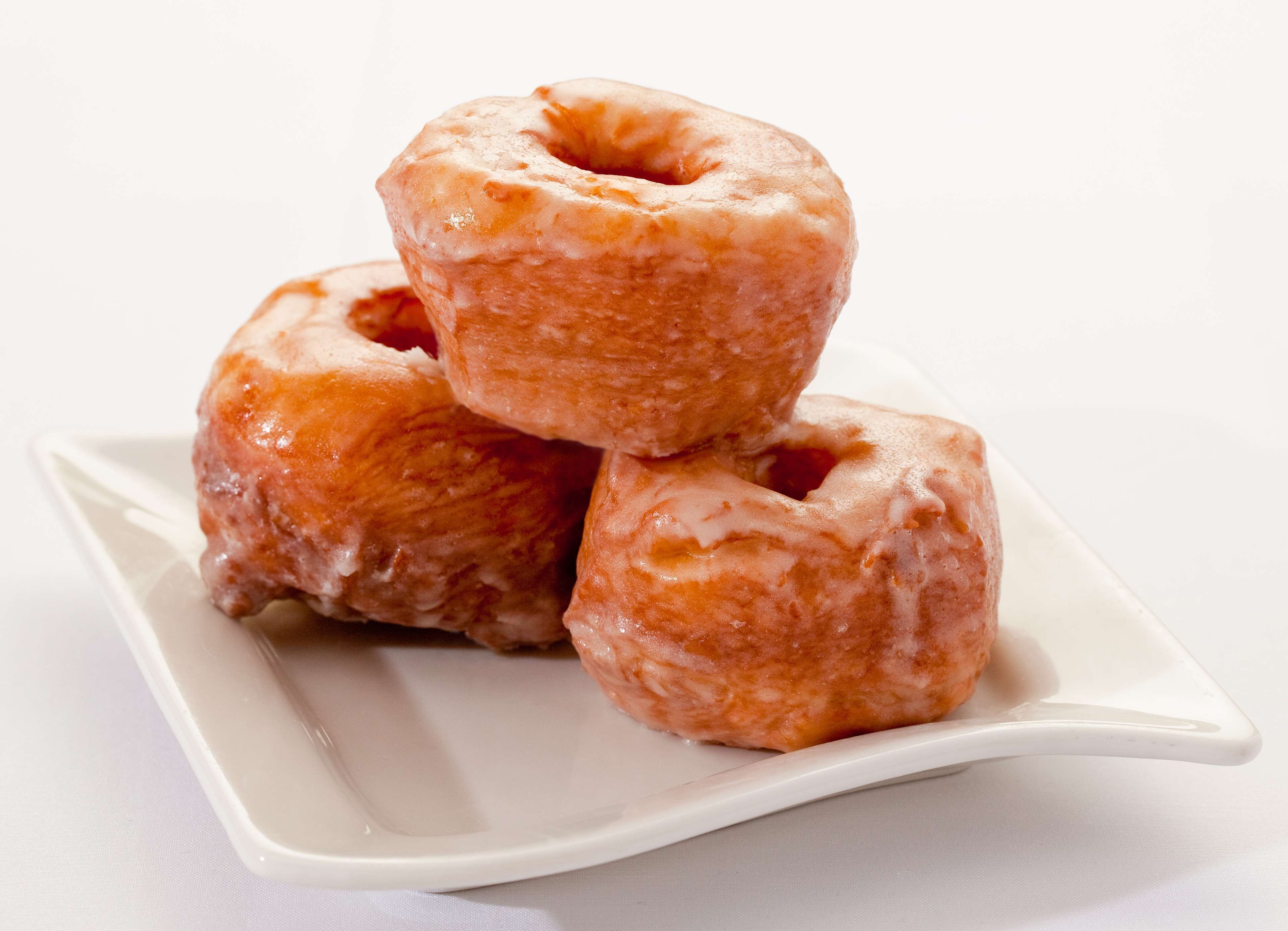 Three glazed donuts stacked on a white plate.