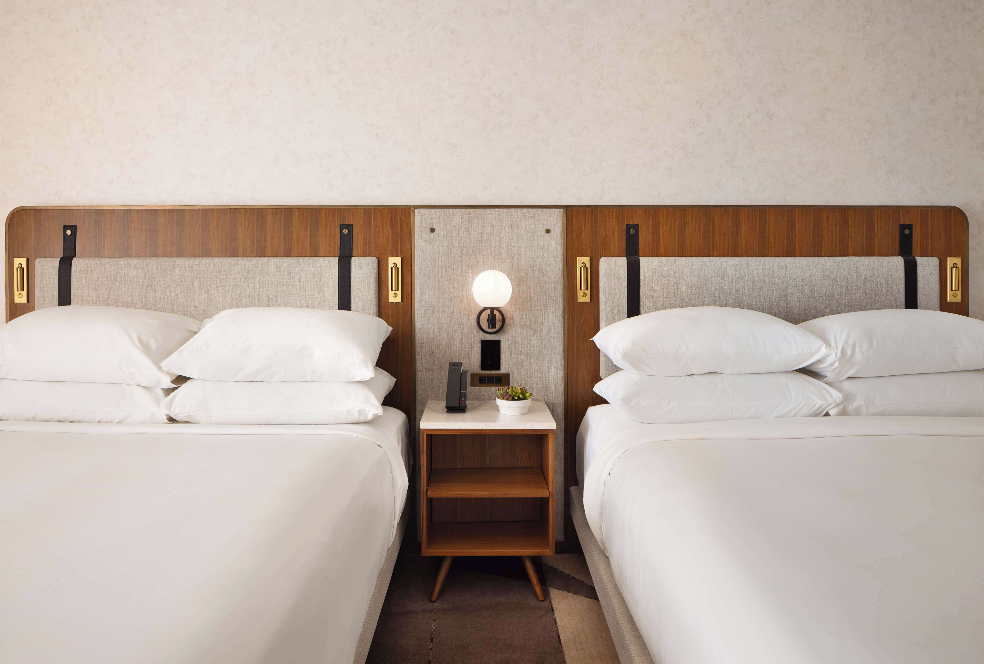 Une chambre d’hôtel avec deux lits, une table de chevet avec une lampe et une petite table avec une plante.
