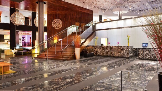 Een moderne lobby met een marmeren vloer, houten details en een trap naar de bovenverdiepingen.