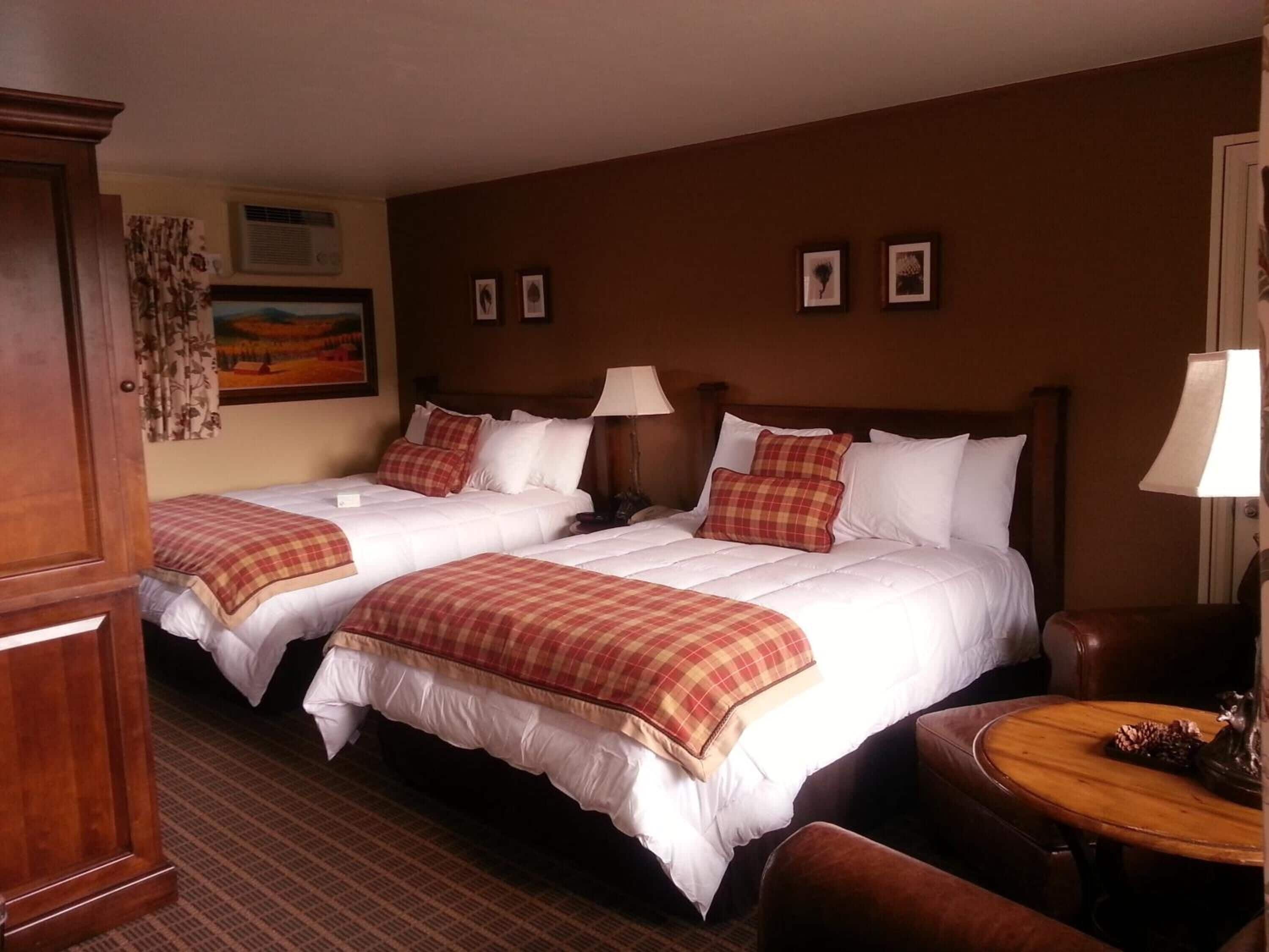 A hotel room with two beds, a wooden desk, a chair, and a small table with a decorative item.